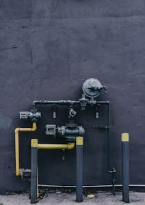 Pipes and machinery against an urban building wall with a gritty industrial look.